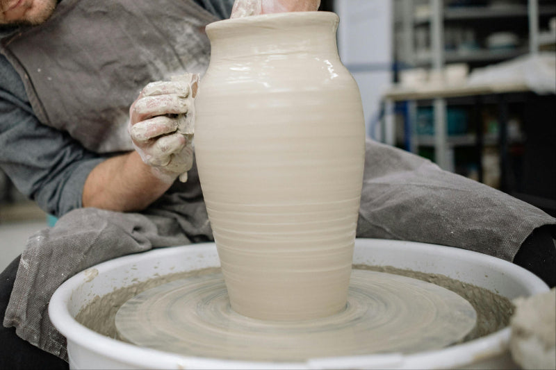 Person working on a ceramic vase on a potter's wheel in the Claya studio workshop.