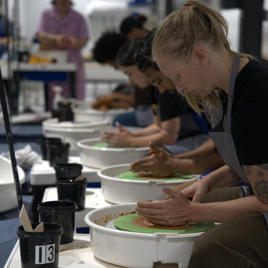 Row of coworkers throwing clay on pottery wheels during a team building event at Claya in RiNo, Denver