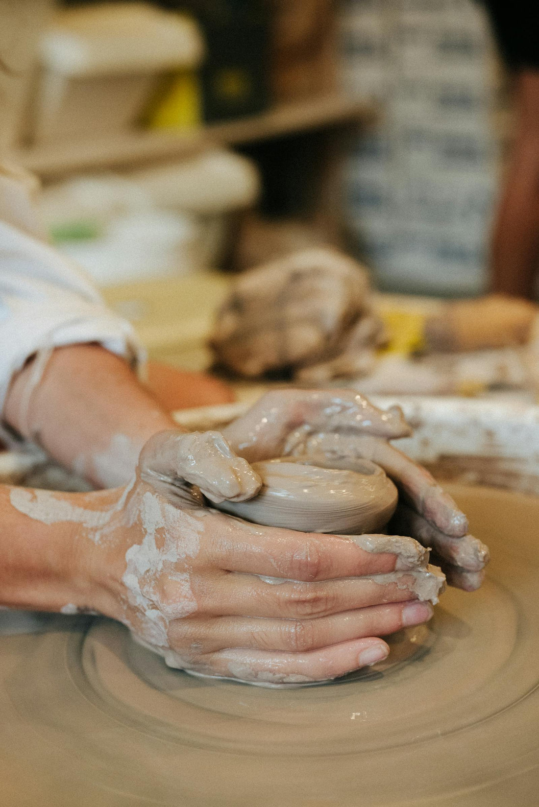 Hands shaping clay on a pottery wheel in a warmly lit studio