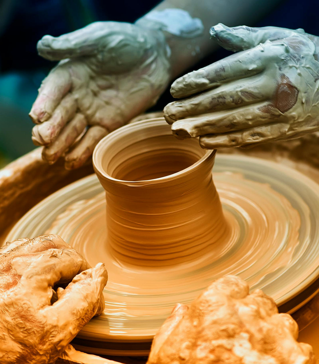 Two people forming clay together on a pottery wheel