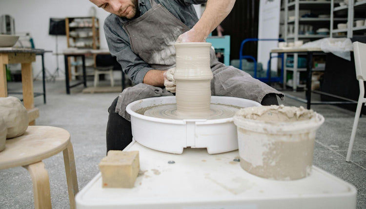 A potter shapes a tall clay piece on the wheel at Claya pottery studio in Denver's RiNo district