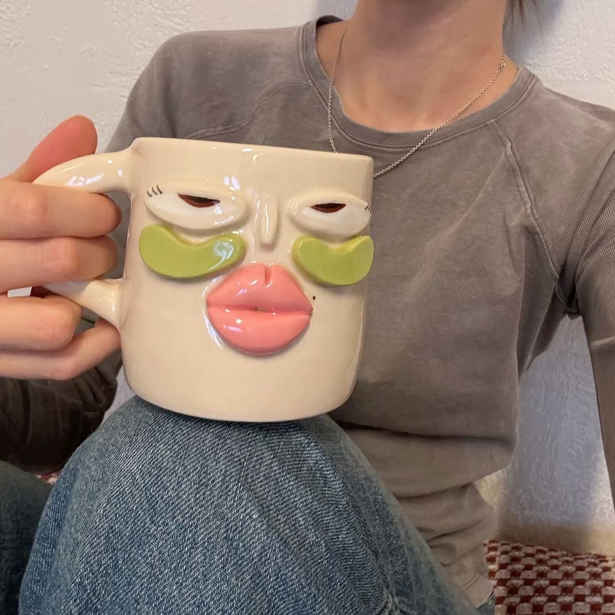 Handbuilt face mug with sculpted eyes and pink lips held in one hand