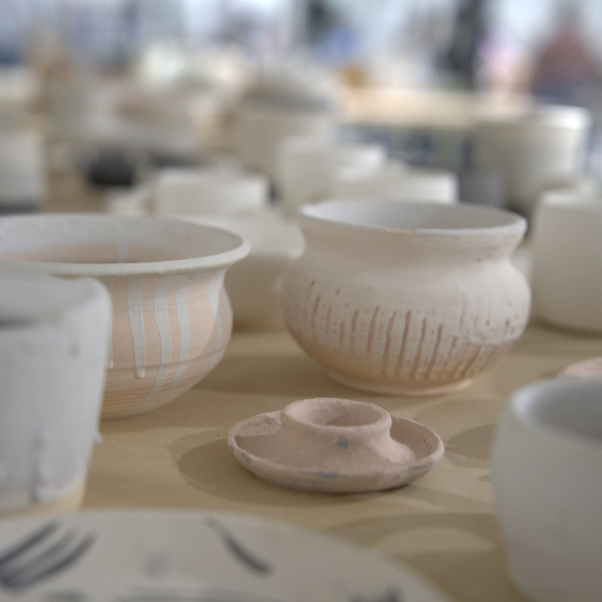 Bisque-fired bowls and plates from wheel classes on a table at Claya Studios in RiNo, Denver