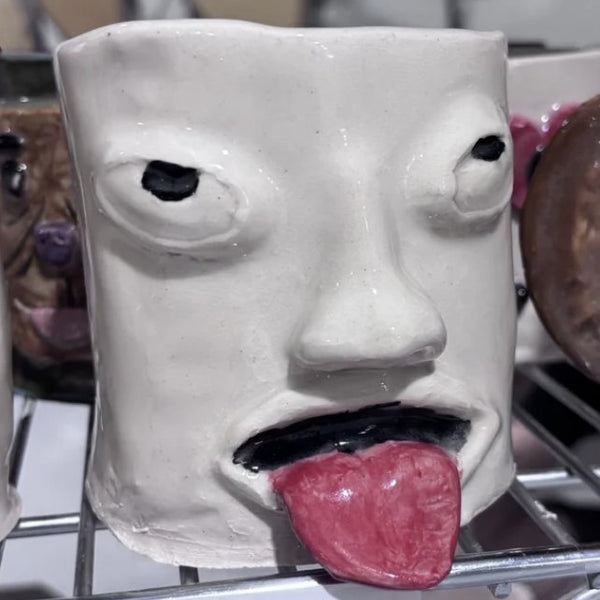 Handbuilt face mug with bulging eyes and pink tongue at Claya pottery studio in Denver