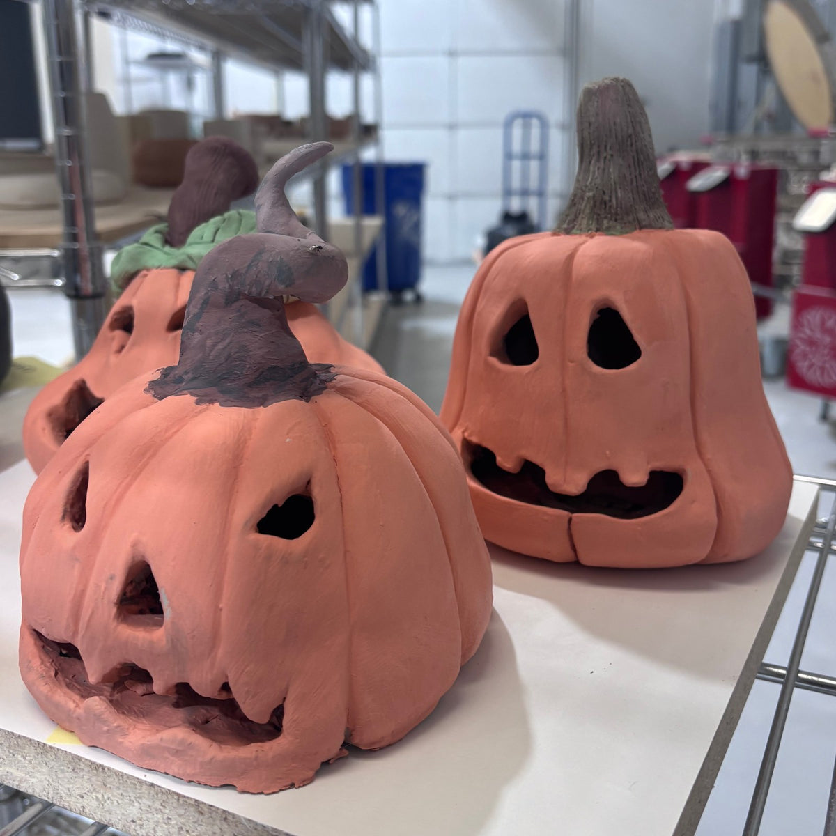 Two terracotta clay pumpkin lanterns with carved jack-o'-lantern faces from the handbuilding workshop at Claya Studios, Denver
