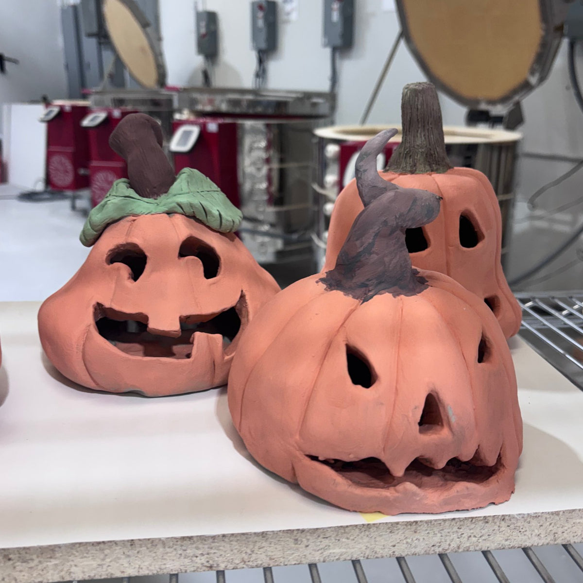 Handbuilt clay pumpkin lanterns, one with a curled witch hat stem and one with a green leaf, in the kiln room at Claya, Denver