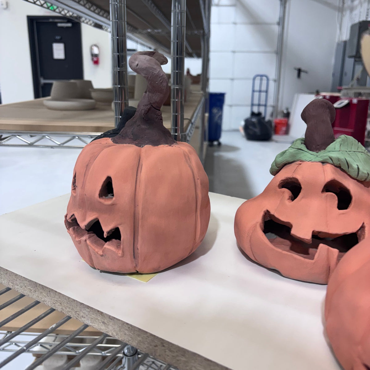 Handbuilt clay jack-o'-lantern with a twisted stem and carved face on a shelf at Claya Studios, 3440 Walnut St, Denver