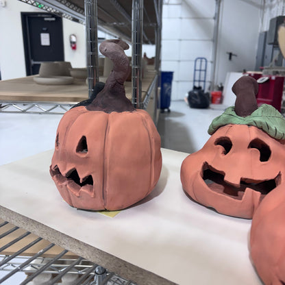 Handbuilt clay jack-o'-lantern with a twisted stem and carved face on a shelf at Claya Studios, 3440 Walnut St, Denver