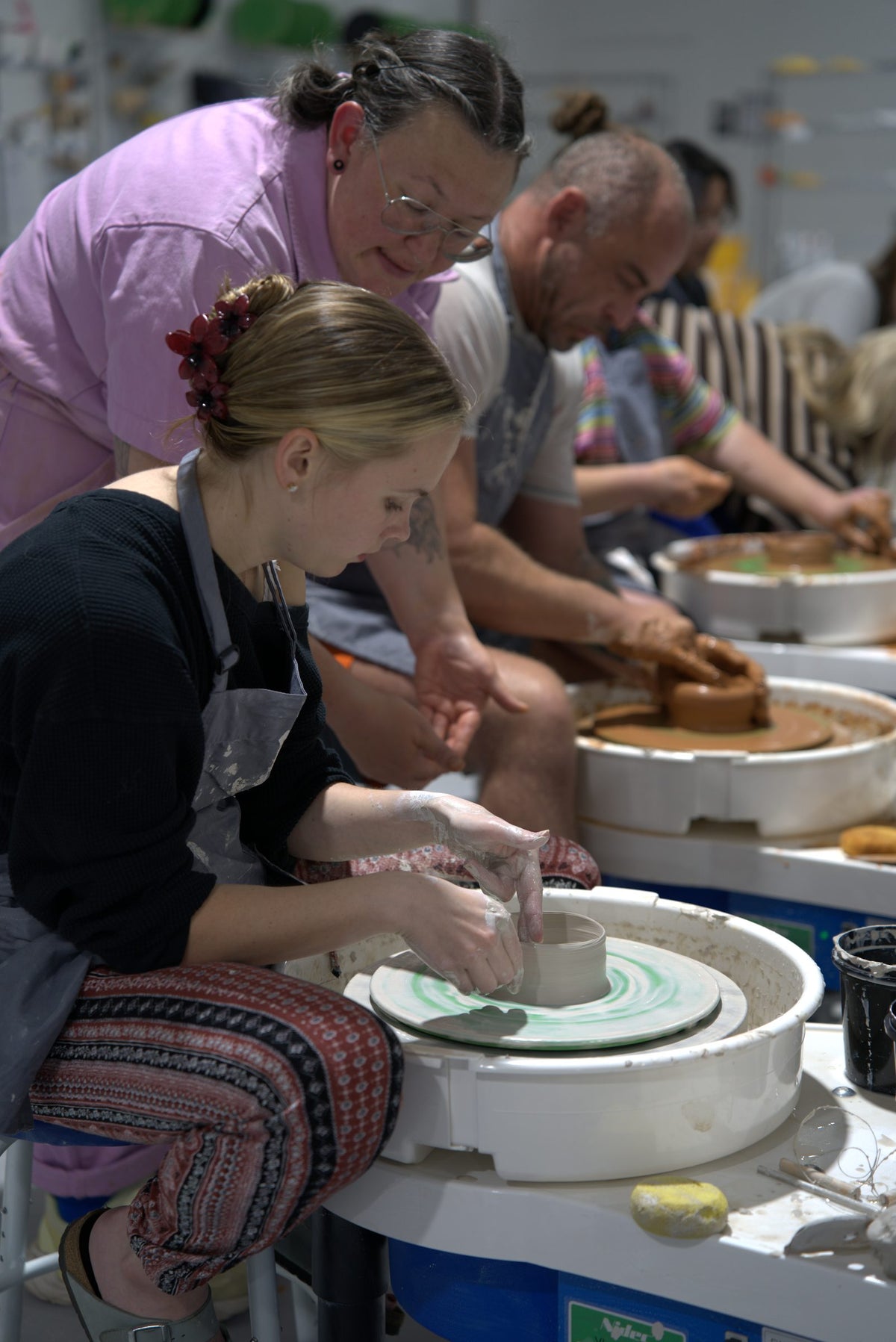 Beginner wheel throwing class at Claya Studios in RiNo, Denver, instructor Caitlin coaching a student at the pottery wheel
