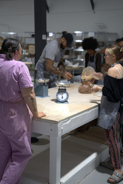 Beginner wheel throwing class at Claya Studios in RiNo, Denver, instructor Caitlin with students wedging clay at the wedging table