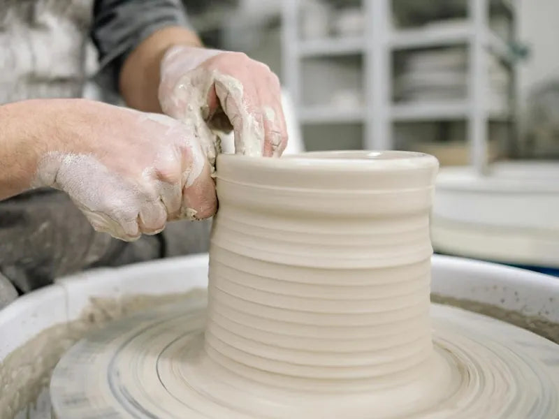 Hands shaping a tall vessel on the pottery wheel at CLAYA during pottery class in Denver