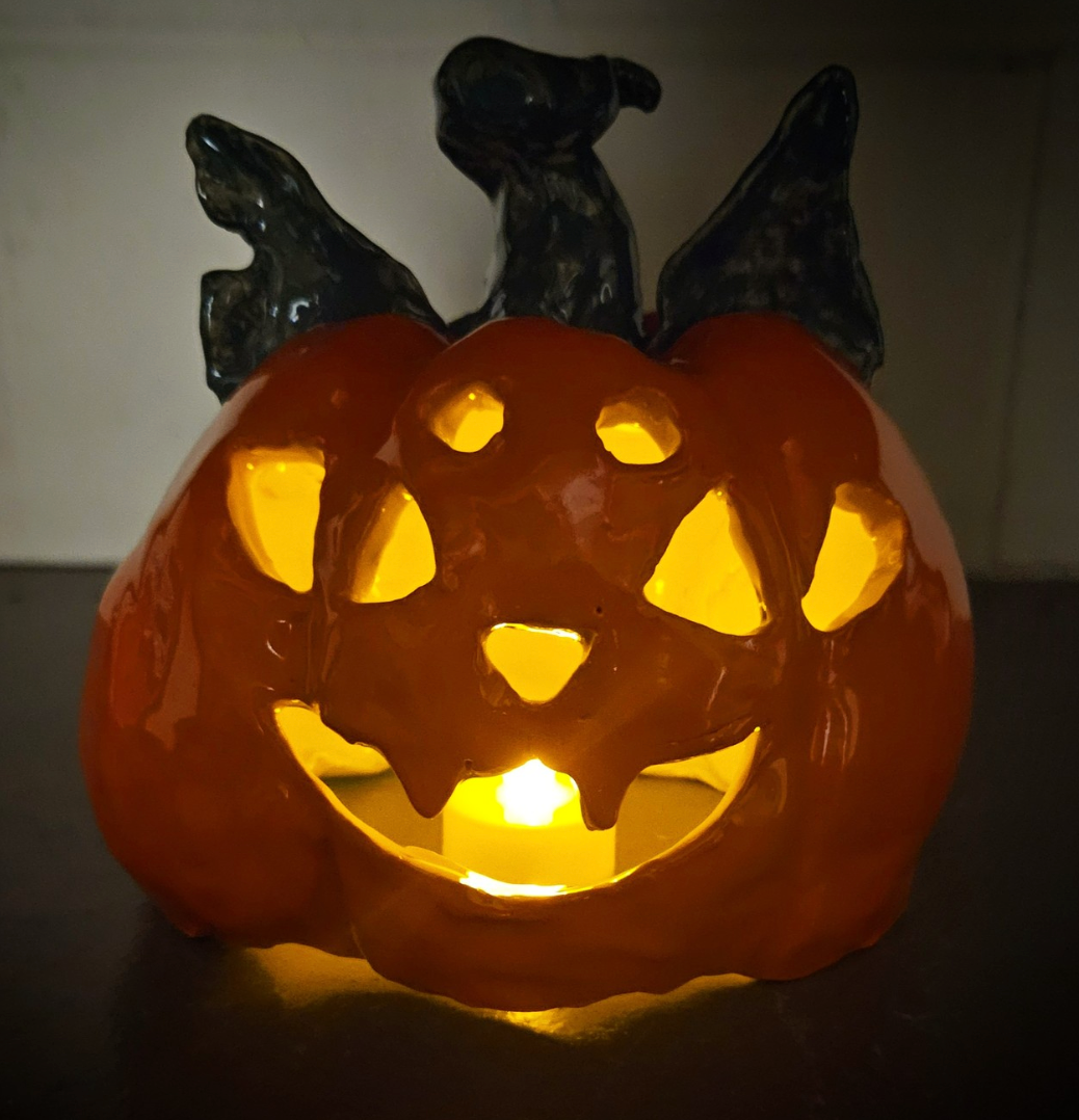 Handmade ceramic jack-o'-lantern glowing with a tea light, made at Claya's Pumpkin Night