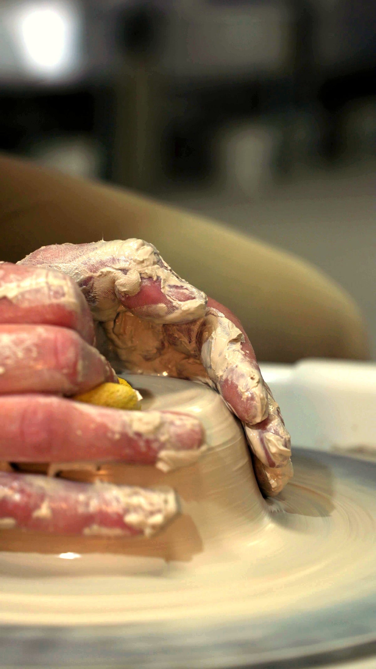 Close-up of clay-covered hands throwing on the wheel at Claya pottery studio in Denver