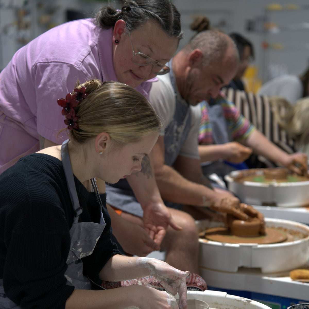 Instructor Caitlin coaching a student throwing on the pottery wheel in a wheel class at Claya Studios in RiNo, Denver