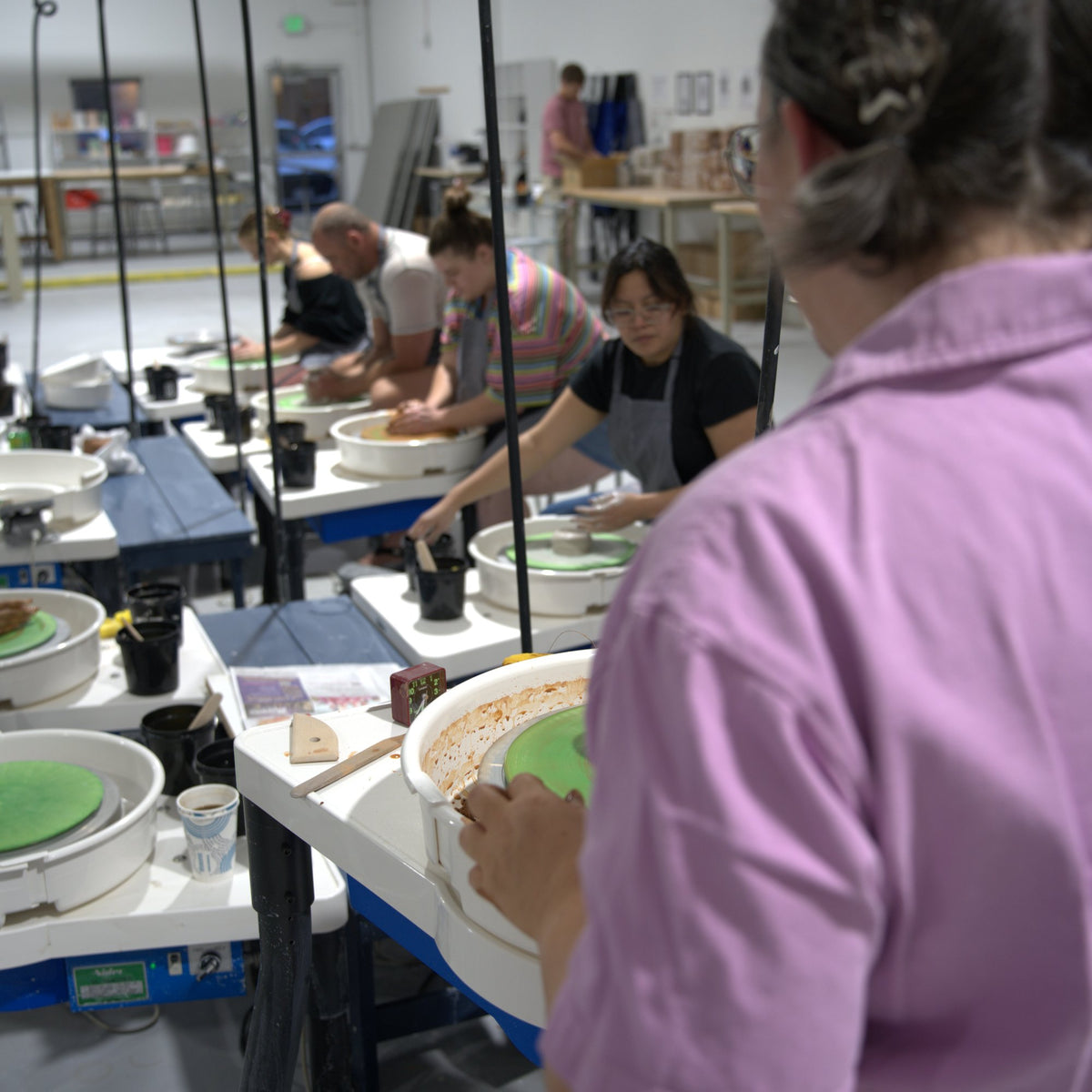 Instructor Caitlin watching over students throwing on pottery wheels at Claya Studios in RiNo, Denver