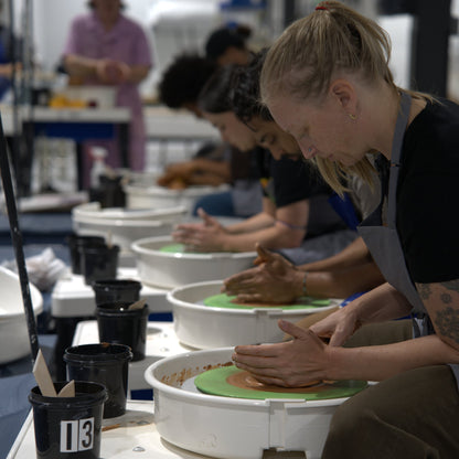 Row of students throwing clay on pottery wheels in a wheel class at Claya Studios in RiNo, Denver