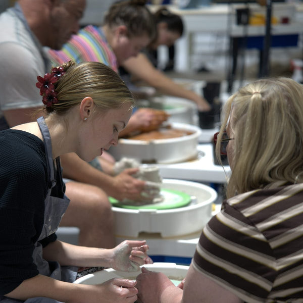 Students throwing side by side on pottery wheels in a class at Claya in RiNo, Denver