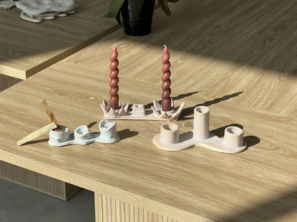 Coil-built ceramic candle holders holding red taper candles on a sunlit table